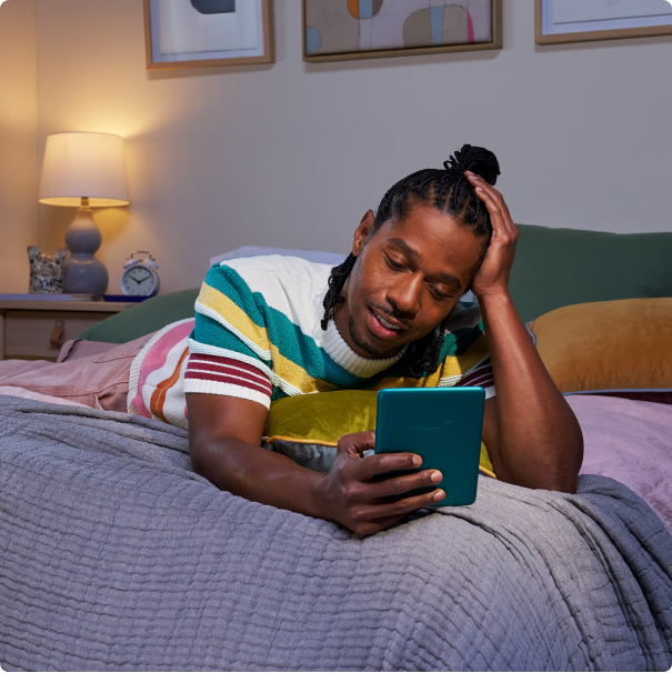 A man lounges in bed while reading his Kindle Paperwhite Signature Edition.