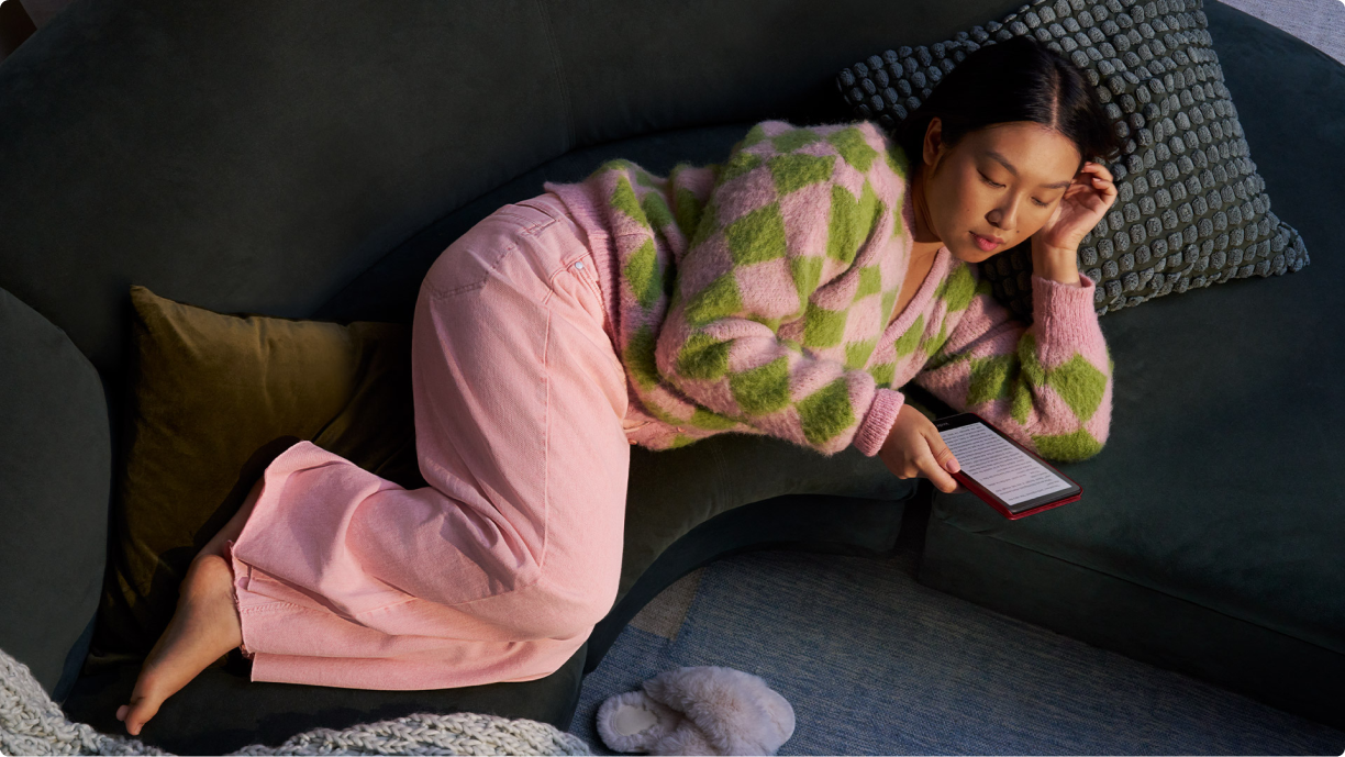 A woman lays on a couch while reading her Kindle Paperwhite Signature Edition.