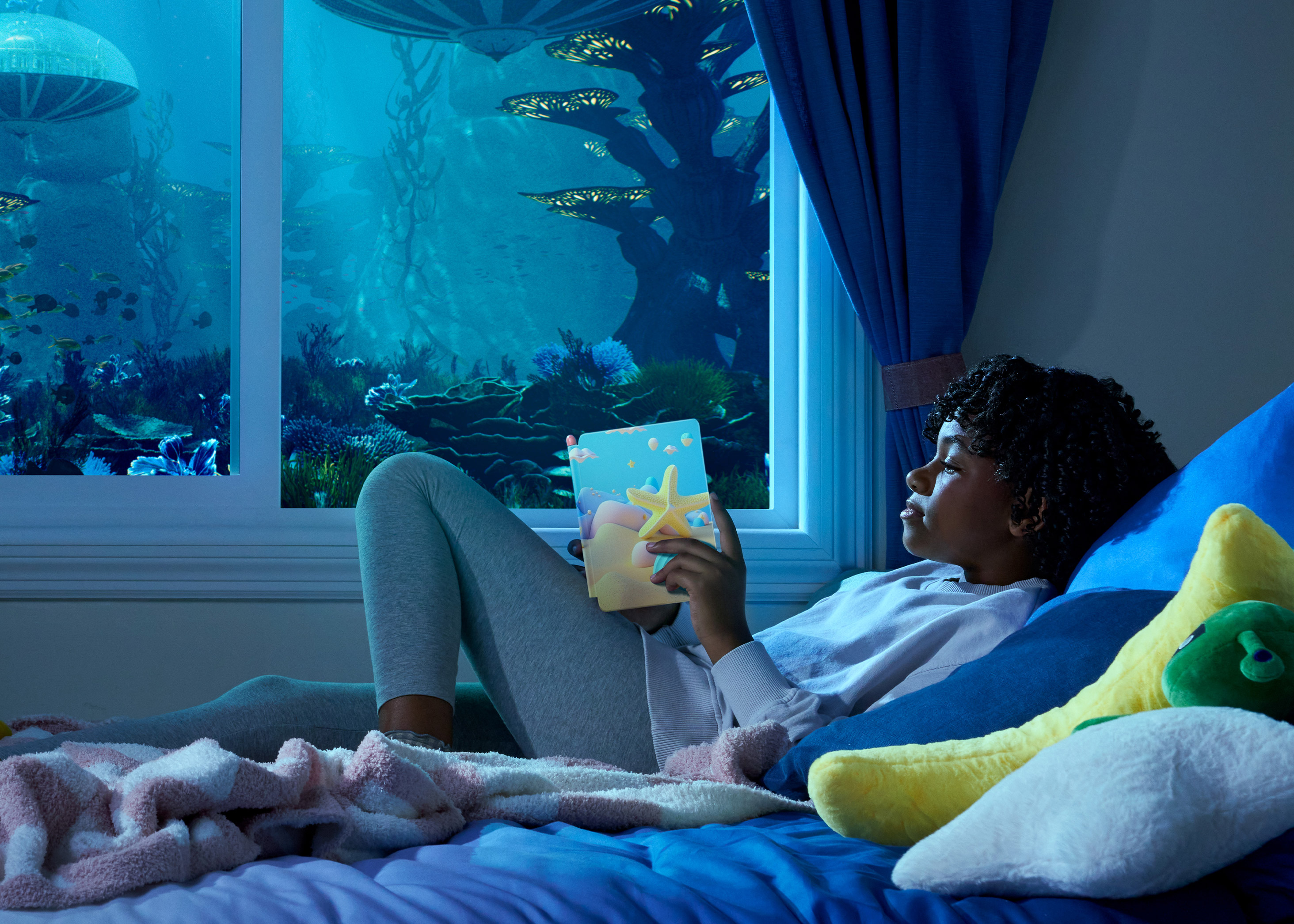 Teen sits in bed reading Kindle Paperwhite Kids in dim lighting. Outside their window is a fantastical underwater world.