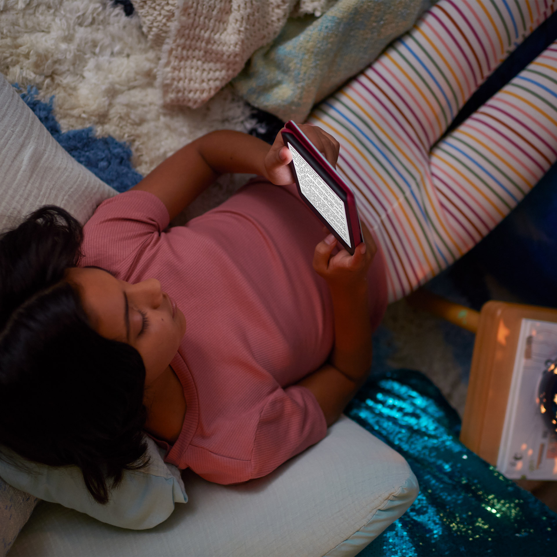In a dimly lit room, child holds Kindle Kids with illuminated screen.