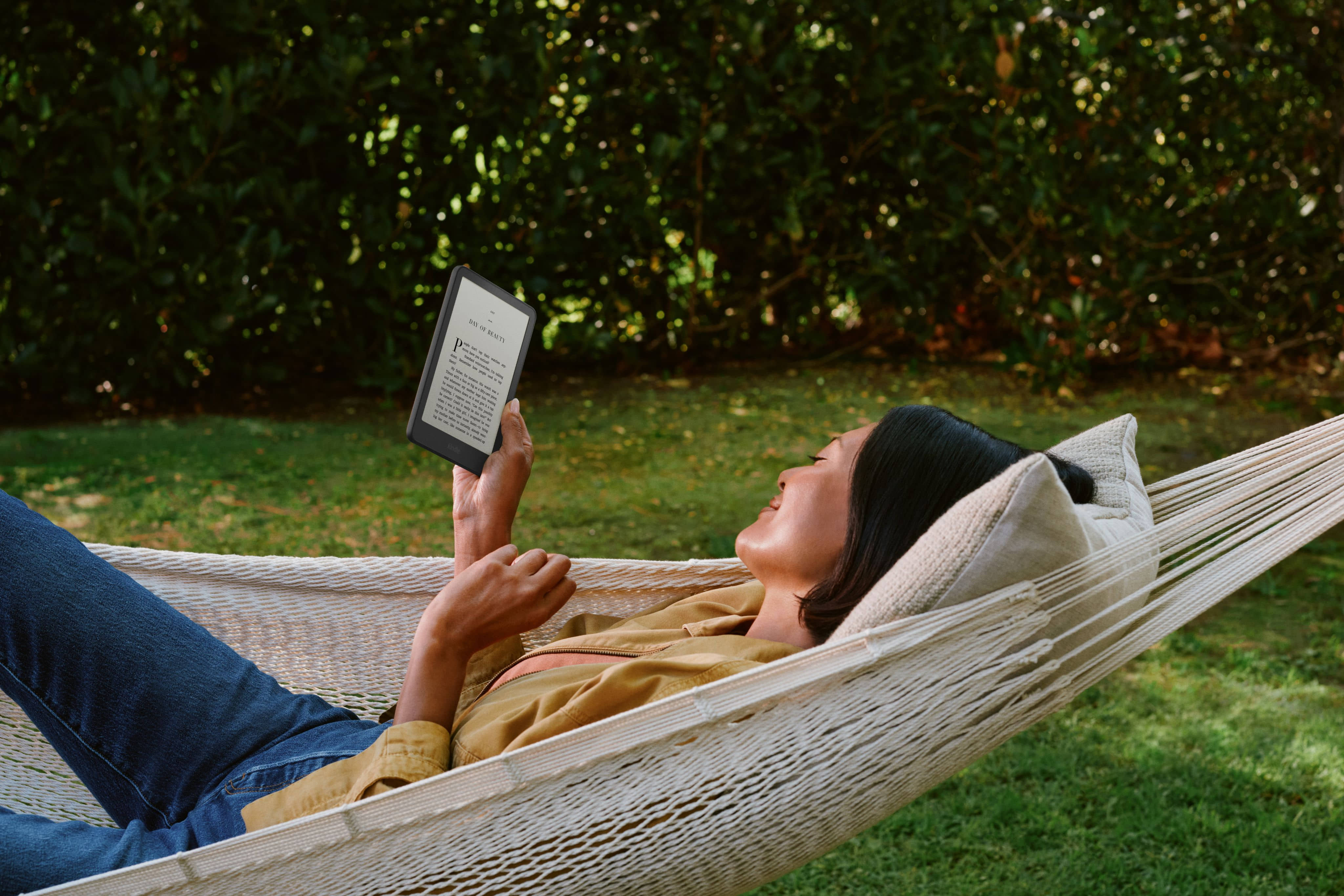Person relaxing in hammock outdoors reading on Amazon Kindle Paperwhite.