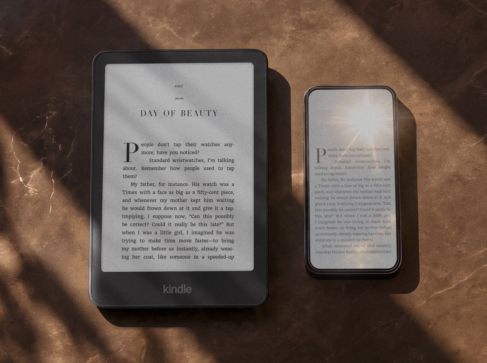 Amazon Kindle Paperwhite e-reader and a mobile displaying text on their screens, placed on a surface with dappled sunlight.