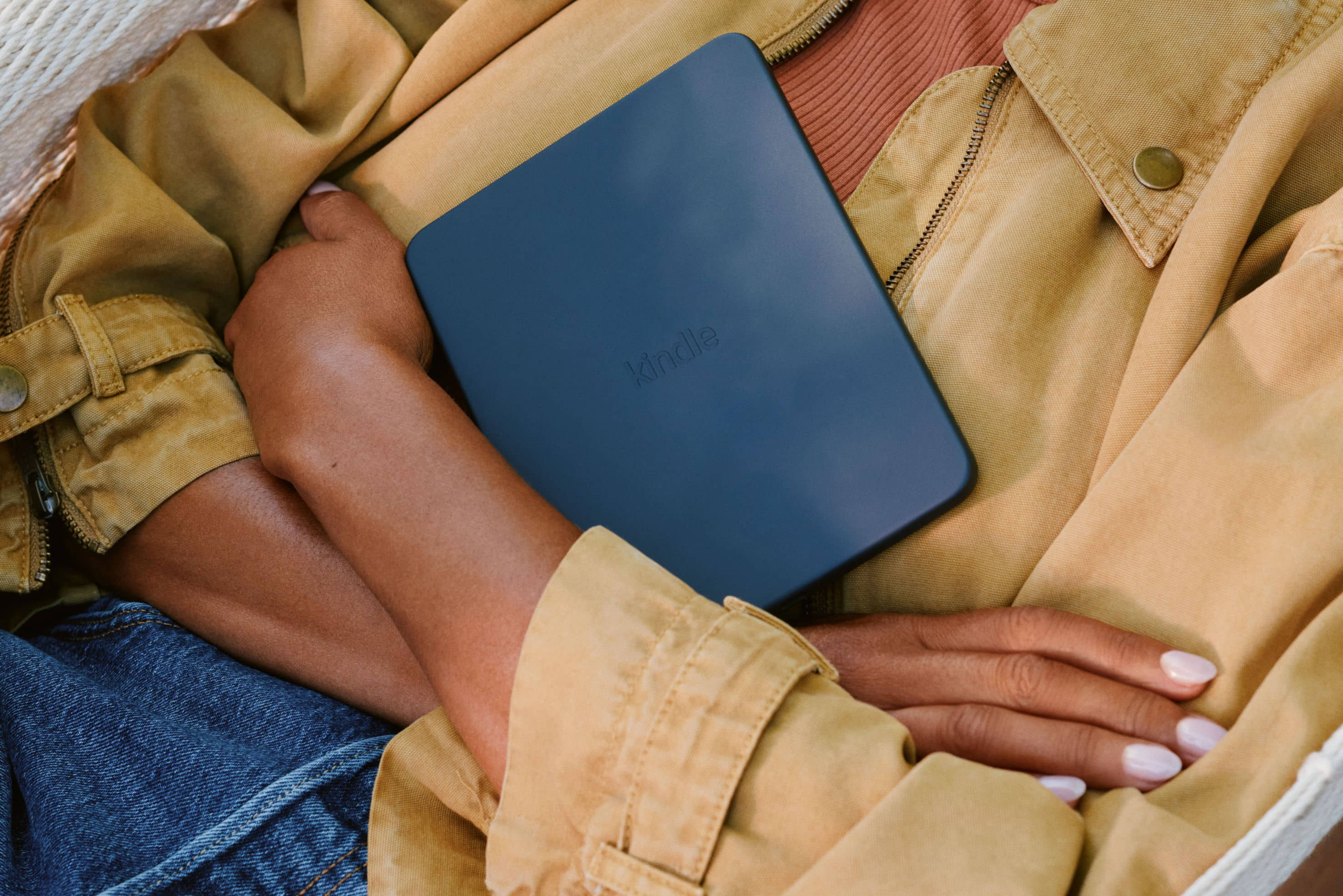 Person holding Amazon Kindle Paperwhite with a dark blue cover while relaxing on a couch.