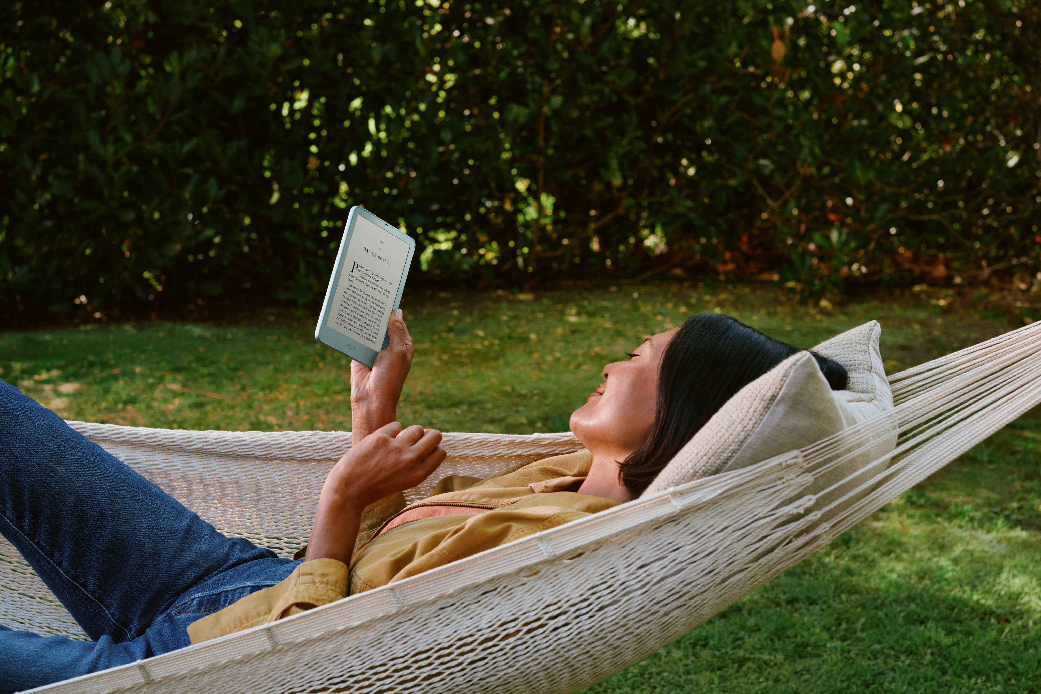 Person relaxing in hammock outdoors reading on Amazon Kindle e-reader with rounded corners.