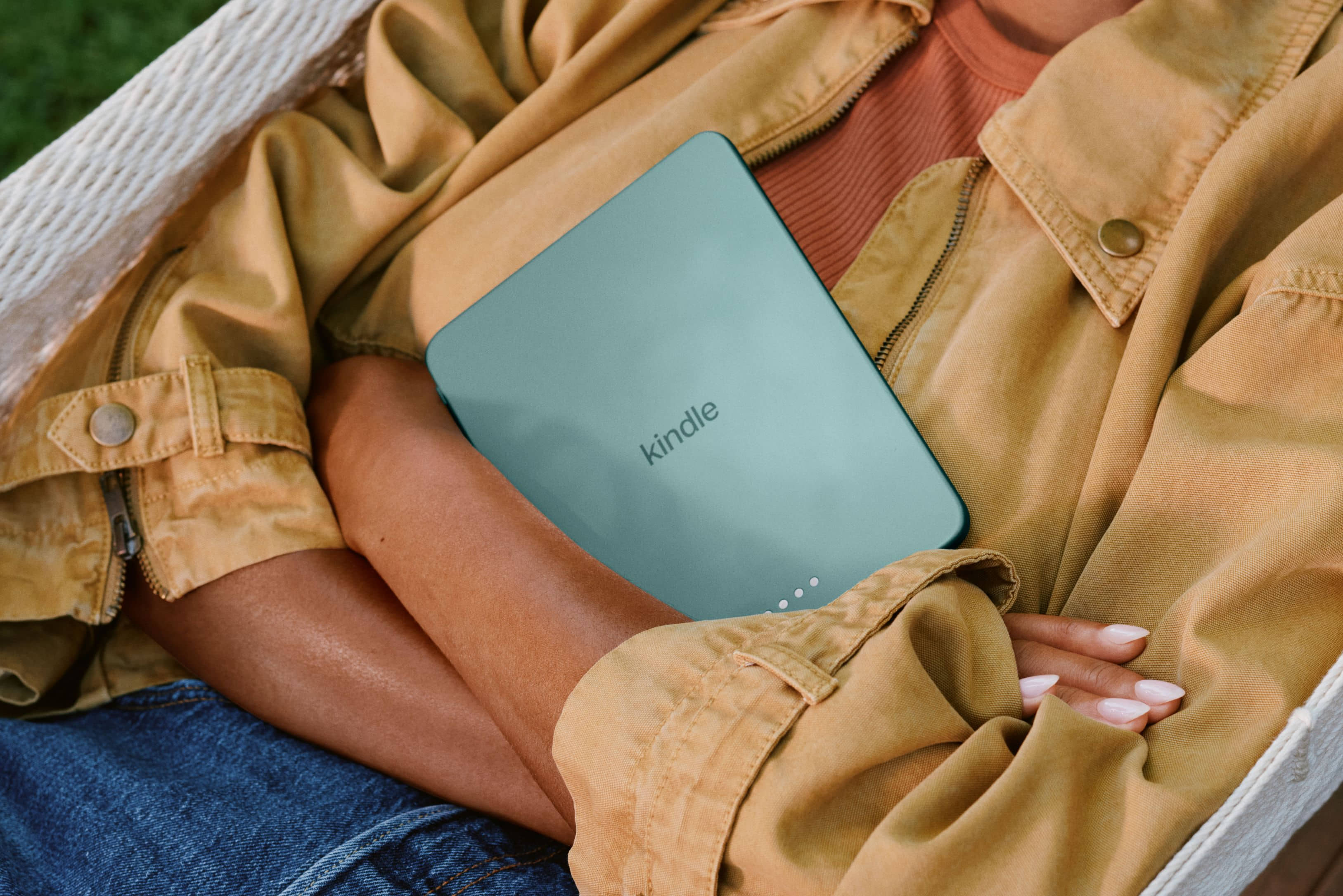 Person relaxing outdoors holding Amazon Kindle e-reader with rounded corners in light blue.