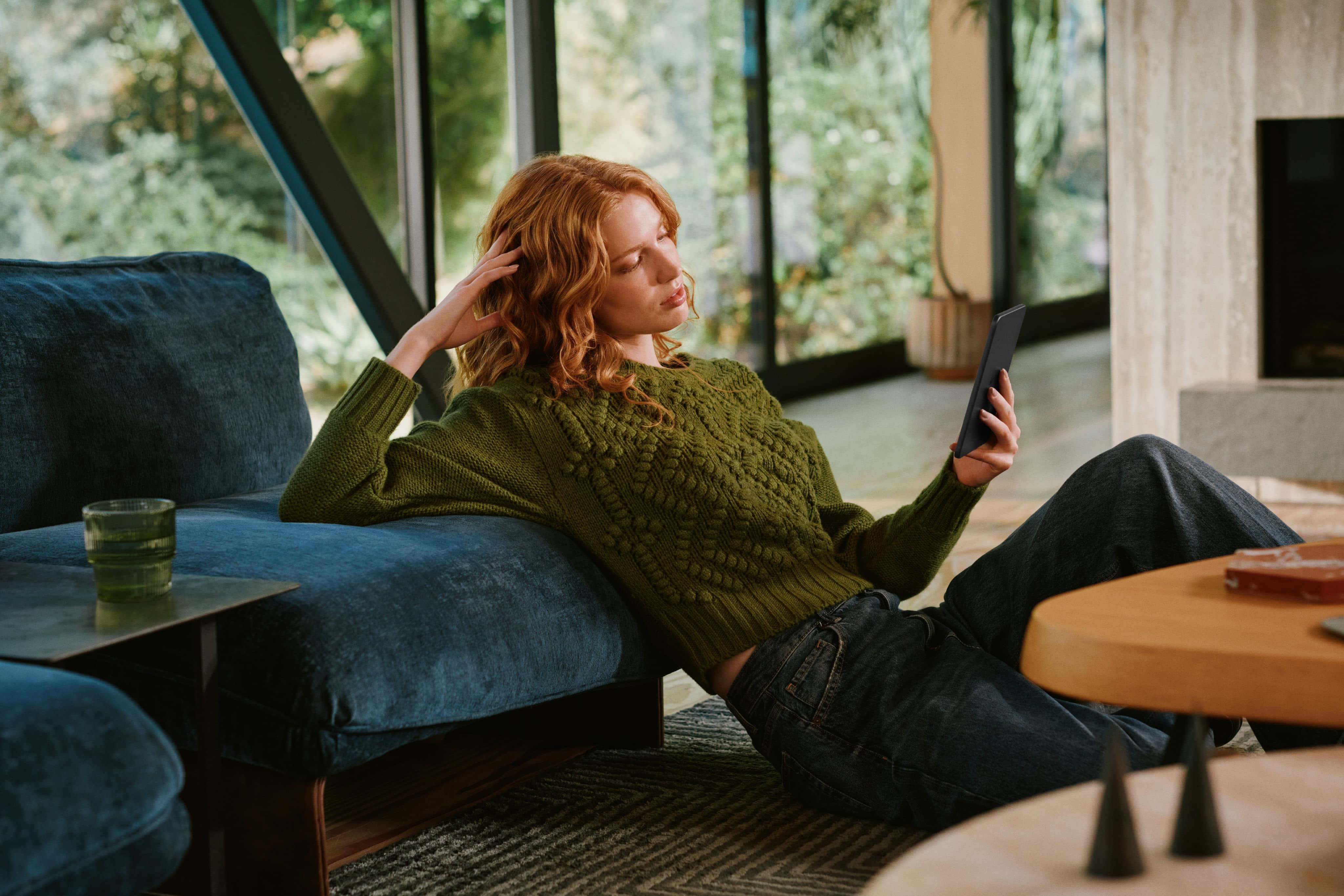 Person relaxing on couch reading on Amazon Kindle in modern living room.