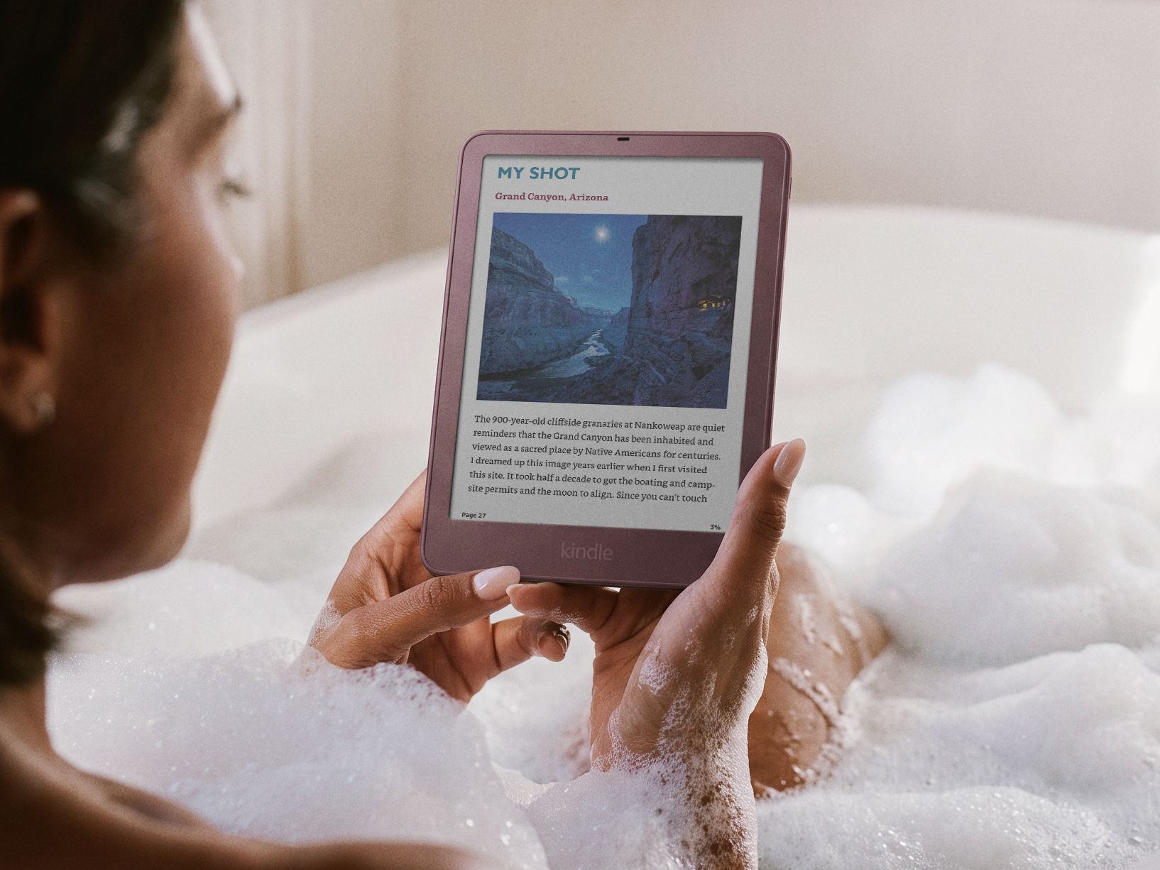 Person in bathtub holding Kindle displaying library of book covers.